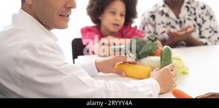 Médecin nutritionniste hispanique consultant un enfant métis avec sa mère afro-américaine au sujet d'une nutrition. Nourriture de légumes - une nouvelle façon pour le bien Banque D'Images