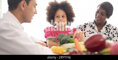 Médecin nutritionniste hispanique consultant un enfant métis avec sa mère afro-américaine au sujet d'une nutrition. Nourriture de légumes - une nouvelle façon pour le bien Banque D'Images