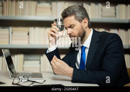 L'homme d'affaires a eu la migraine touche sa tête à cause de la douleur. Homme responsable avec un gros mal de tête travaillant sur un ordinateur portable. Travailleur indépendant ou responsable chez de Banque D'Images