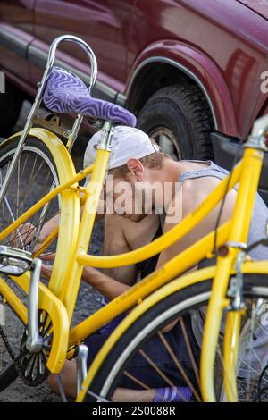 Homme réparant un vélo jaune à l'extérieur, assis près d'une voiture garée Banque D'Images