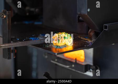 Verre fondu fusionnant avec des fragments colorés sur un tuyau de soufflage, le studio de soufflage de verre travaille en cours Banque D'Images