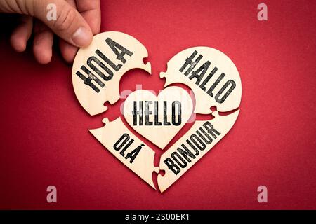 Bonjour dans différentes langues. Puzzle en bois en forme de coeur sur fond rouge. Banque D'Images