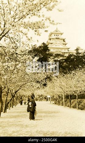 Château d'Osaka au milieu des cerisiers en fleurs : sentier de cerisiers en fleurs avec porteur de kimono traditionnel près du château historique dans un cadre printanier. Osaka, Japon. années 1890 Banque D'Images