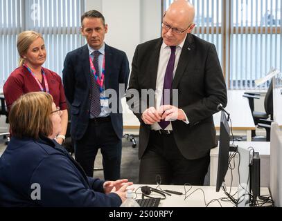 Le premier ministre John Swinney accompagné de Valerie Guilford, gestionnaire d’appels, en tant que Patrick Rafferty, directeur adjoint des soins infirmiers NHS24, et Julie Lindsay, gestionnaire des services cliniques NHS24, regardent, lors de sa visite au centre d’appels NHS 24 à Dundee, où il a rencontré le personnel et visité les installations avant la période des fêtes. Date de la photo : lundi 23 décembre 2024. Banque D'Images