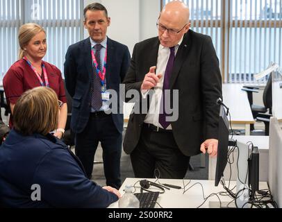 Le premier ministre John Swinney accompagné de Valerie Guilford, gestionnaire d’appels, en tant que Patrick Rafferty, directeur adjoint des soins infirmiers NHS24, et Julie Lindsay, gestionnaire des services cliniques NHS24, regardent, lors de sa visite au centre d’appels NHS 24 à Dundee, où il a rencontré le personnel et visité les installations avant la période des fêtes. Date de la photo : lundi 23 décembre 2024. Banque D'Images
