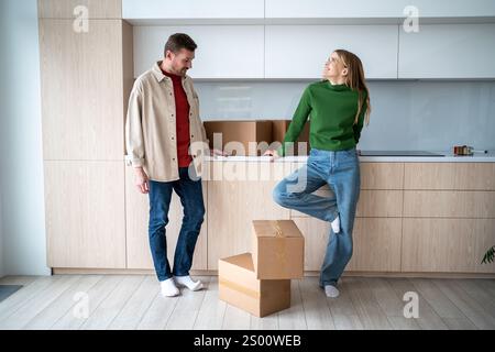 Heureuse femme rêvant regarde se tient avec l'homme près de boîtes en carton dans la cuisine tout en déménageant dans la nouvelle maison Banque D'Images