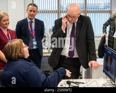 Le premier ministre John Swinney accompagné de Valerie Guilford, gestionnaire d’appels, en tant que Patrick Rafferty, directeur adjoint des soins infirmiers NHS24, et Julie Lindsay, gestionnaire des services cliniques NHS24, regardent, lors de sa visite au centre d’appels NHS 24 à Dundee, où il a rencontré le personnel et visité les installations avant la période des fêtes. Date de la photo : lundi 23 décembre 2024. Banque D'Images