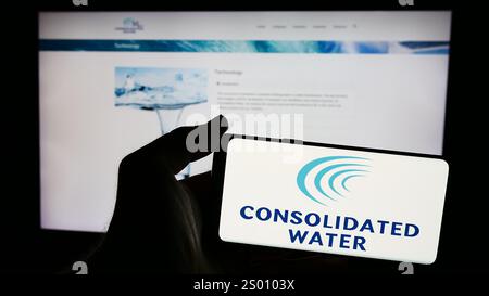 Dans cette illustration photo, une personne tient un smartphone avec le logo de la société de dessalement d'eau de mer Consolidated Water Co. Ltd en face du site Web. Banque D'Images