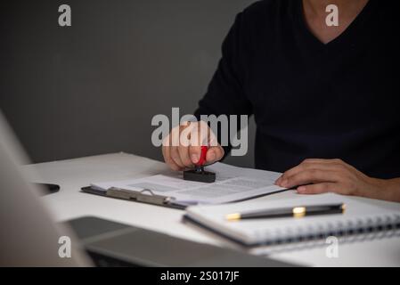 Homme d'affaires estampillant un document officiel pour approbation, symbolisant l'autorité, la validation et la conformité dans le travail administratif. Banque D'Images