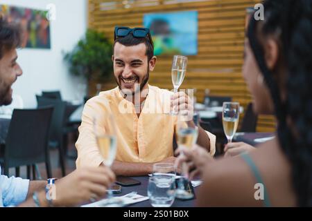 Jeune homme souriant profitant d'une célébration en plein air avec des amis, levant un verre de champagne dans une atmosphère joyeuse et festive. Banque D'Images