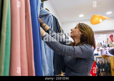 Cliente parcourant des vêtements colorés sur des cintres dans un magasin de détail, sélectionnant des vêtements élégants pour sa garde-robe Banque D'Images