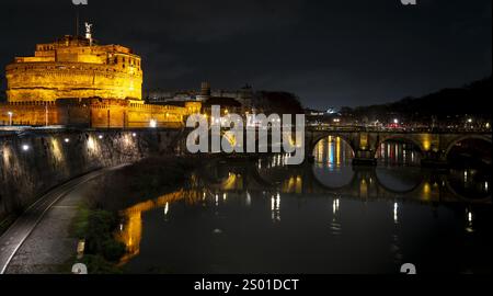 Une vue nocturne du Castel Sant'Angelo à Rome, illuminé contre le ciel sombre. Le Tibre reflète les lumières dorées du château, avec un pont en th Banque D'Images