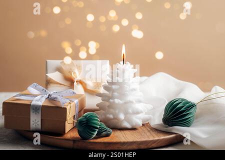 Bougie brûlante blanche festive, boîtes cadeaux et petites boules en nid d'abeille en papier sur fond beige avec lumières de Noël. Banque D'Images