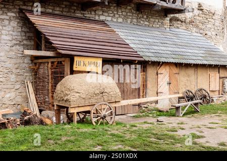 Un chariot en bois avec du foin est garé devant un bâtiment. Le bâtiment a un panneau jaune sur elle qui dit "Kapita". La scène a un rustique et ancien Banque D'Images