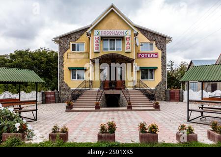 Un grand bâtiment jaune avec un panneau rouge sur le côté. Le bâtiment a un toit vert et un auvent blanc. Il y a plusieurs plantes en pot et bancs dehors Banque D'Images