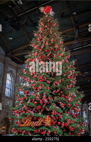 Zurich, Suisse - 24 novembre 2024 : arbre de Noël emblématique Lindt à Zurich SBB Hauptbahnhof orné d'ornements rouges et de décorations en chocolat Banque D'Images