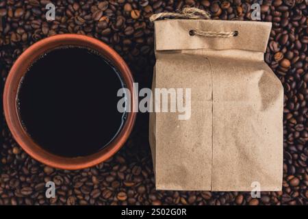 Une vue de dessus d'une tasse de café en céramique remplie de café noir à côté d'un sac en papier kraft, entouré de grains de café torréfiés. Banque D'Images