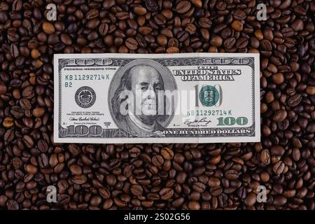 Billet de cent dollars placé sur une surface de grains de café torréfiés, représentant le coût du café, du commerce ou des concepts financiers. Banque D'Images