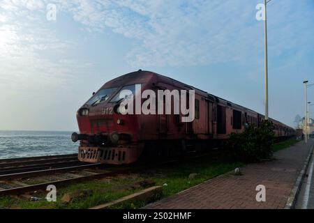 Colombo. 18 décembre 2024. Cette photo prise le 18 décembre 2024 montre un train en bord de mer à Colombo, Sri Lanka. La ligne de chemin de fer côtière, située sur la côte ouest du Sri Lanka et à proximité de l'océan Indien, est une ligne ferroviaire importante dans ce pays insulaire. C'est également une attraction touristique célèbre, où la côte droite, les calèches sans portes, et la belle vue sur la mer tout au long du voyage permettent aux gens d'obtenir l'expérience unique de style Ceylan. Crédit : Gayan Sameera/Xinhua/Alamy Live News Banque D'Images