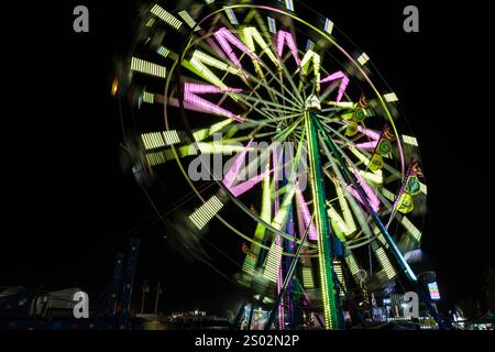 Un tour de carnaval avec des lumières vives et des gens dessus tourne dans l'obscurité. Le trajet est une grande roue, et il est éclairé par des néons, creat Banque D'Images