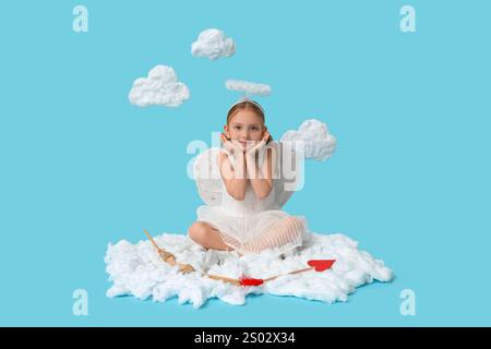 Mignonne petite fille habillée comme Cupidon avec flèche et arc assis sur un nuage sur fond bleu. Célébration de la Saint-Valentin Banque D'Images