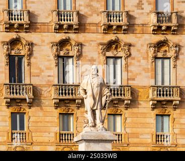 Une statue en marbre d'un homme distingué se dresse devant un bâtiment orné de balcons décoratifs et de fenêtres. La statue est détaillée et capture Banque D'Images