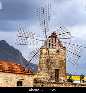 Un moulin à vent historique avec de grandes lames en bois, sur fond de montagnes et de ciel nuageux. Le moulin à vent dispose d'une structure en pierre et d'un rouge- Banque D'Images