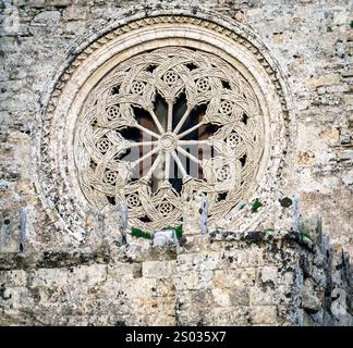 Une fenêtre en pierre détaillée avec des sculptures complexes, avec un motif circulaire et des motifs floraux, sertie contre un mur de pierre antique. Banque D'Images
