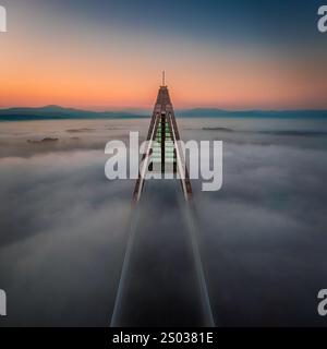 Budapest, Hongrie - vue aérienne de l'un des piliers du pont Megyeri sur le Danube recouvert d'un épais brouillard d'automne au coucher du soleil de bleu et d'or Banque D'Images
