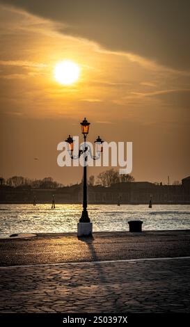 Un coucher de soleil serein sur un plan d'eau, avec un lampadaire vintage au premier plan. Le soleil projette une lueur chaude, éclairant la scène avec un l doux Banque D'Images