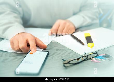 Une personne examine les données de crypto-monnaie sur un smartphone et prend des notes tout en analysant les tendances du marché dans un environnement de bureau contemporain. Banque D'Images