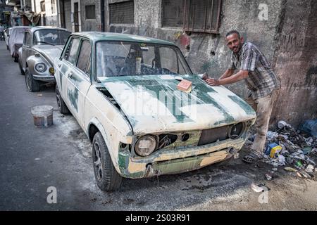 Un réparateur automobile sable une vieille voiture dans la rue d'Alexandrie, en Égypte, la préparant pour la peinture. Savoir-faire automobile urbain. Banque D'Images