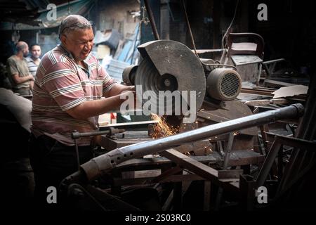 Un artisan travaille avec un outil de coupe dans un atelier extérieur à Alexandrie, en Egypte, créant des étincelles. Capturer l'essence de l'artisanat traditionnel Banque D'Images