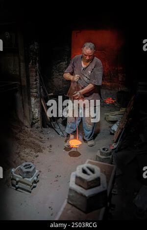 Ouvrier de fonderie dans un atelier à Alexandrie, Egypte, coulant du métal fondu dans un cadre traditionnel. Une image de fondateur en laiton reflète l'artisanat local Banque D'Images