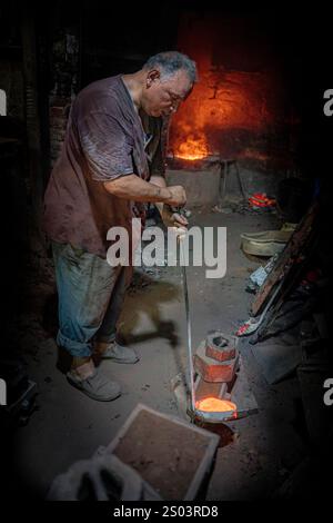 Ouvrier de fonderie dans un atelier à Alexandrie, Egypte, coulant du métal fondu dans un cadre traditionnel. Une image de fondateur en laiton reflète l'artisanat local Banque D'Images