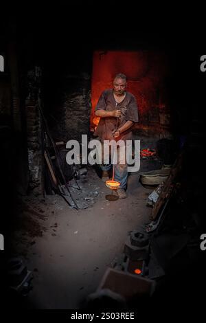 Ouvrier de fonderie dans un atelier à Alexandrie, Egypte, coulant du métal fondu dans un cadre traditionnel. Une image de fondateur en laiton reflète l'artisanat local Banque D'Images