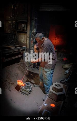 Ouvrier de fonderie dans un atelier à Alexandrie, Egypte, coulant du métal fondu dans un cadre traditionnel. Une image de fondateur en laiton reflète l'artisanat local Banque D'Images