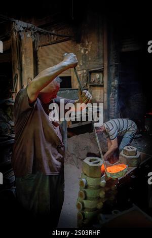 Ouvrier de fonderie dans un atelier à Alexandrie, Egypte, coulant du métal fondu dans un cadre traditionnel. Une image de fondateur en laiton reflète l'artisanat local Banque D'Images