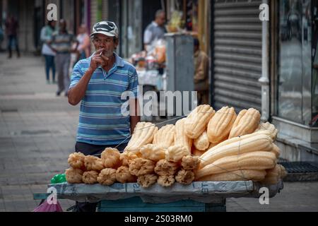Vendeur de rue à Alexandrie, Egypte, fumant tout en vendant des loofahs naturels. La scène capture l'essence de la vie quotidienne en milieu urbain. Banque D'Images