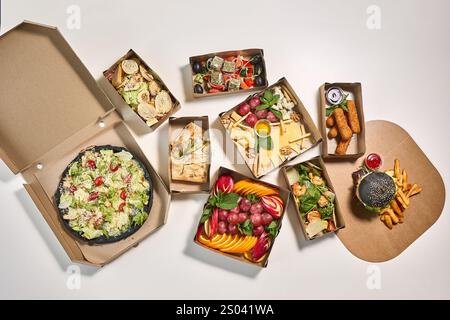 Une pose à plat de divers plats à emporter dans des boîtes en carton, y compris pizza, salade, fromage, fruits, et un hamburger. Banque D'Images