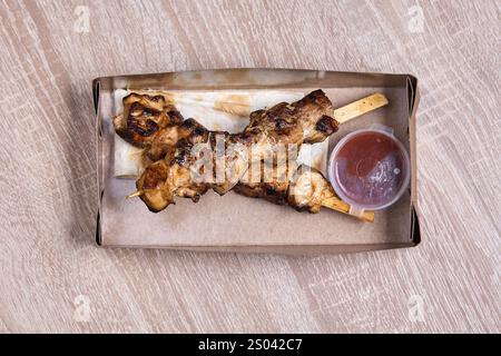 Deux brochettes de poulet grillé avec sauce dans une boîte en carton à emporter. Banque D'Images