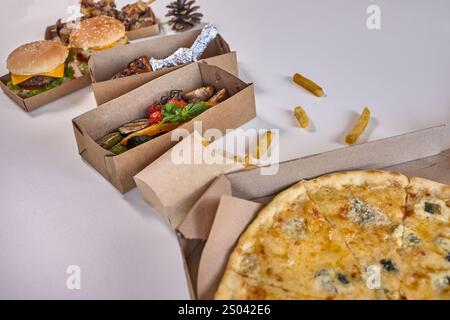 Un plat de divers plats à emporter dans des boîtes en carton, y compris pizza, hamburgers, poulet grillé et légumes. Banque D'Images