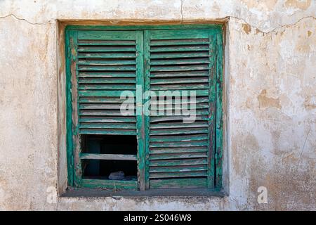 Un volet rustique en bois vert sur un vieux mur altéré à Lavrio, en Grèce, met en valeur le charme de la pourriture avec de la peinture écaillée et des textures naturelles Banque D'Images