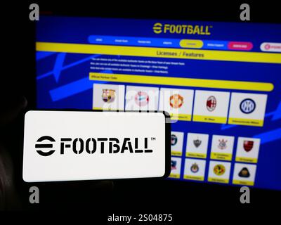 Dans cette illustration photo, une personne tient un smartphone avec le logo du jeu vidéo de football eFootball (Konami) en face du site Web. Banque D'Images