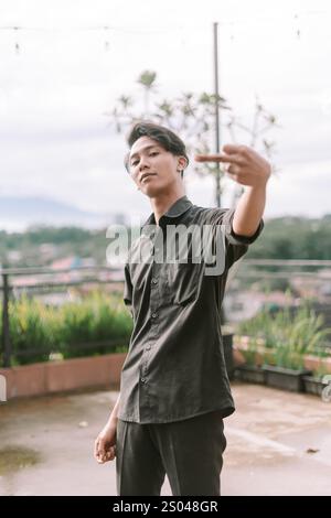 Homme d'Asie du Sud-est faisant un geste de la main avec une expression audacieuse. Mise au point sur la main et le visage, cadre extérieur, lumière naturelle. Concept de rébellion, attitude Banque D'Images