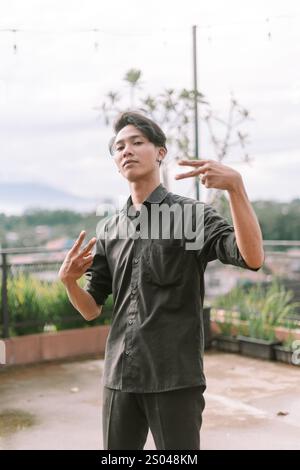 Homme d'Asie du Sud-est faisant un geste de la main avec une expression audacieuse. Mise au point sur la main et le visage, cadre extérieur, lumière naturelle. Concept de rébellion, attitude Banque D'Images