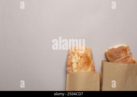 Sacs en papier avec baguettes fraîches sur table grise, vue de dessus. Espace pour le texte Banque D'Images