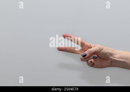 vue détaillée de la main d'une femme avec deux doigts soulevés sur un fond gris lisse. Ce geste commun peut signifier la paix, la victoire, ou simplement le Banque D'Images