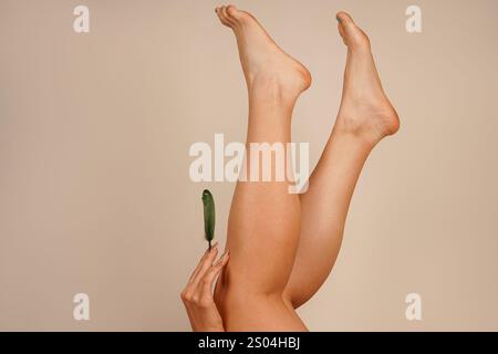 Les jambes d'une femme sont levées vers le haut tandis que sa main déplace une plume sur sa peau. Cette image se concentre sur le processus de soin, mettant en évidence la douceur A. Banque D'Images