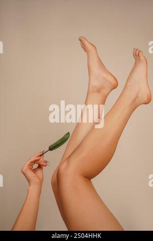 Les jambes d'une femme sont levées vers le haut tandis que sa main déplace une plume sur sa peau. Cette image se concentre sur le processus de soin, mettant en évidence la douceur A. Banque D'Images